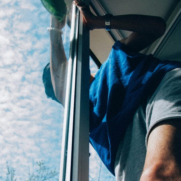 Eine Person reinigt ein Fenster im Freien unter einem hellen Himmel.